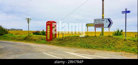 Along The Mourne Coastal Route, in County Down, Northern Ireland, an old disused red telephone box near road signs for Kearney and Portaferry. Stock Photo