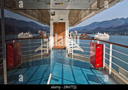 Reflecting on Carnival Luminosa Cruise Ship window, anchored Cruise Boat & port, with Juneau shoreline in the distance, Alaska. Stock Photo