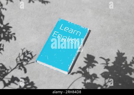 English textbook on a cement table on a clear day with shadows. English language learning. English grammar. Learn English book for language learning. Stock Photo