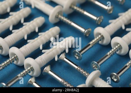Many metal screws with white dowels on blue background, closeup Stock Photo