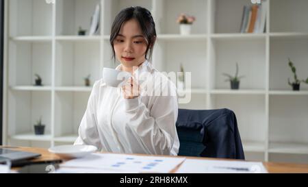 A professional Asian businesswoman focuses on reading, analyzing, and examining financial reports, working at her desk in the office. Stock Photo