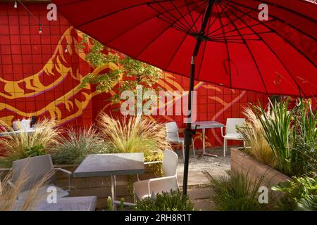 Cozy outdoor restaurant seating area with red umbrella and plants Stock Photo
