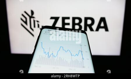 Mobile phone with website of US company Zebra Technologies Corporation on screen in front of business logo. Focus on top-left of phone display. Stock Photo
