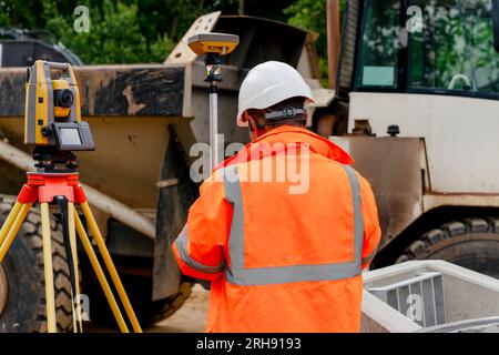 Surveyor site engineer with total positioning station on the construction site of the new road construction with construction machinery and materials Stock Photo