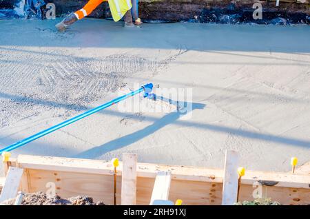 Builder using a steel pan and trowel to spread, level and smooth the wet concrete Stock Photo