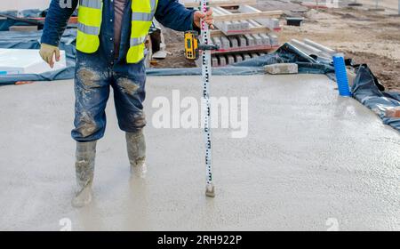 Builder pouring ground floor slab of a new house with wet ready-mix concrete, levelling it and checking the level Stock Photo