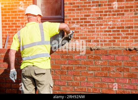 Hard working bricklayer lays bricks on cement mix on construction site. Fight housing crisis by building more affordable houses concept Stock Photo