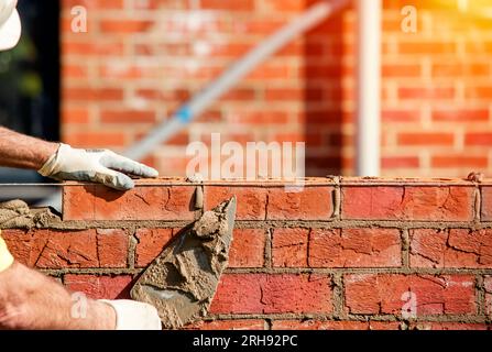 Hard working bricklayer lays bricks on cement mix on construction site. Fight housing crisis by building more affordable houses concept Stock Photo