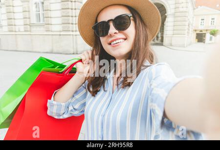Young elegant fashionable woman taking a selfie with her new fashionable purchase in shopping bags. Stock Photo