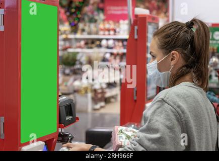 Woman in protective face mask using self-service digital display in retail place. Stock Photo