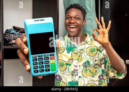 image of a black african man standing excitedly while holding a pos machine, pos terminal, technology device Stock Photo