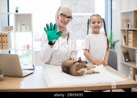 Girl and vet in pet grooming glove smiling at camera Stock Photo