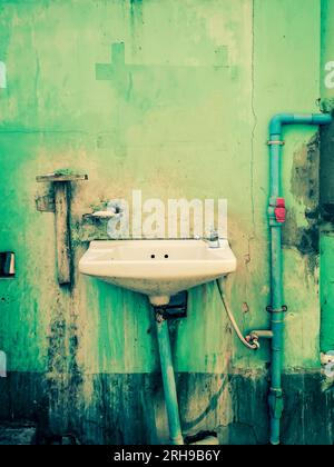 Old sink on a green delapidated wall Stock Photo