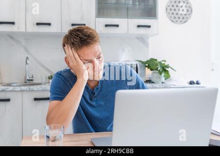 Tired exhausted man freelancer working at home, tired of working in a laptop, overworked, needs rest and break. Male on remote job tired from working Stock Photo