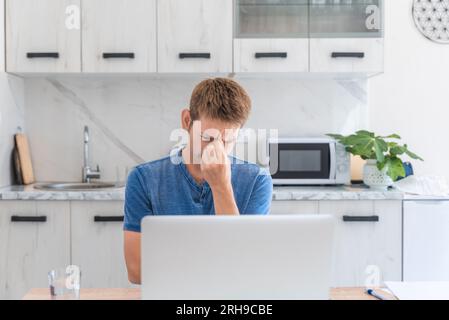 Tired exhausted man freelancer working at home on laptop, overworked, needs rest and break. Stressed male feeling pain, eye fatigue, rubbing dry Stock Photo