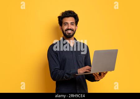 IT Business. Indian Man With Laptop In Hands Posing On Yellow Background Stock Photo