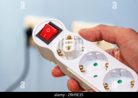 Plug adapter connected in an electrical splitter with European sockets and a red switch button in hand Stock Photo