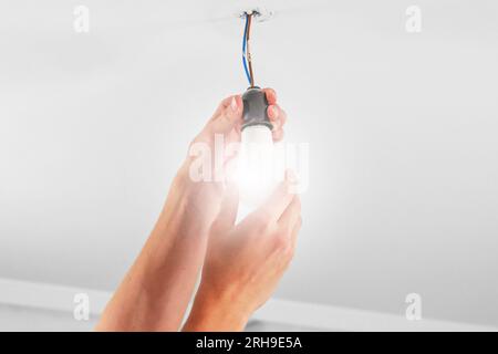 Replacing an glowing electrical energy saving white light bulb close up. Conceptual view Stock Photo