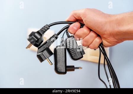 A bunch of disconnected electrical plugs with cables in a hand in room. Saving electricity concept Stock Photo
