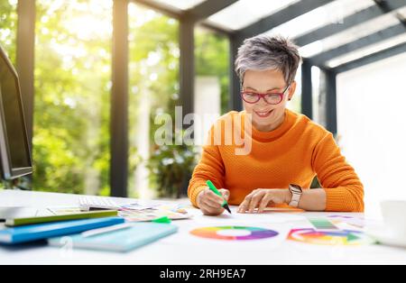 Happy attractive mature woman fashion designer working at home office Stock Photo