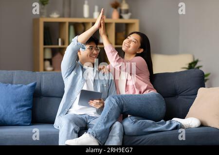 Japanese Couple Using Digital Tablet Giving High Five At Home Stock Photo