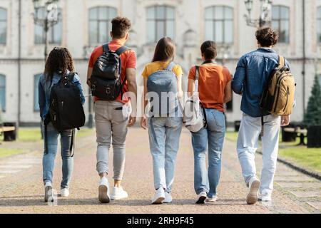 Group of five students with backpacks walking at university campus together Stock Photo