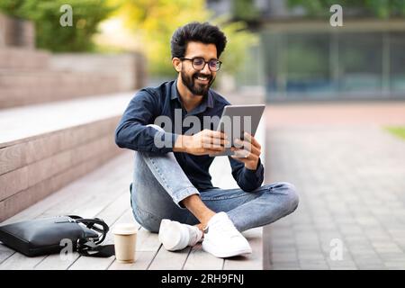 Positive indian guy resting at park after work, using tablet Stock Photo