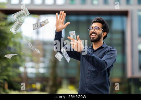 Overjoyed rich young indian businessman throwing money dollar banknotes Stock Photo