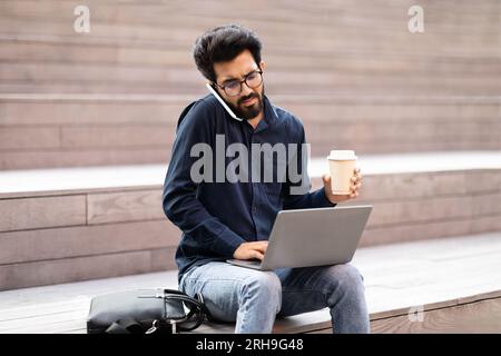 Eastern businessman working remotely at park, talking on phone Stock Photo