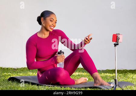 Black woman trainer recording tutorial in gadren, using phone Stock Photo