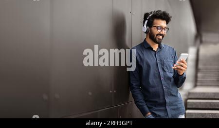 Happy indian guy hipster using phone and headphones on street Stock Photo