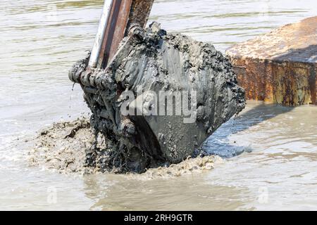 Dredging the bottom of water area, view of the bucket of the floating excavator full of mud Stock Photo