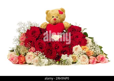 Bouquet of rose flowers isolated on white background. The roses are aranged as a heart shape. A teddy bear is sitting ontop of the flowers. Stock Photo