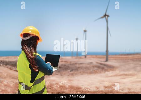 Female engineer working with computer tablet on wind alternative energy generator farm site - Industry and technology concept Stock Photo