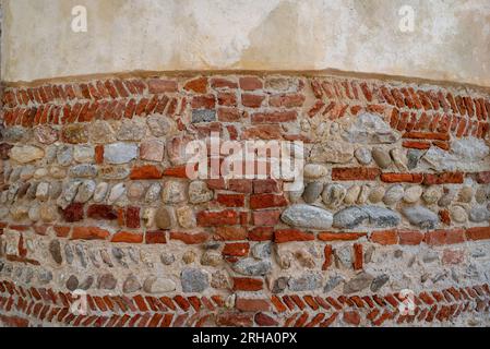 Textured ancient curved shaped wall made of tones and red bricks arranged in herringbone pattern with plastered upper part, background with copy space Stock Photo