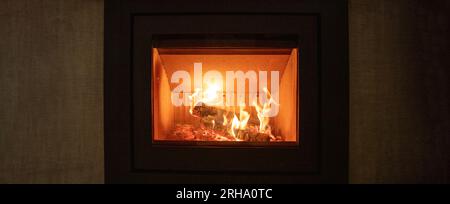 Energy fireplace on a wall, fire flames and burning wood logs in a stove, warm home in winter, front view, banner Stock Photo