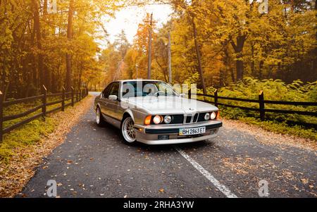Wide angle shot of silver BMW 6-series E24 coupe. Three quarter view of 1980-s 'sharknose' BMW with round headlights on golden autumn day in a forest. Stock Photo