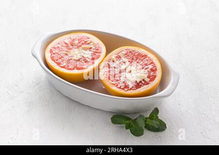 White ceramic baking dish red grapefruit halves smeared with butter on a light gray table. Cooking step, cooking delicious dessert. Stock Photo
