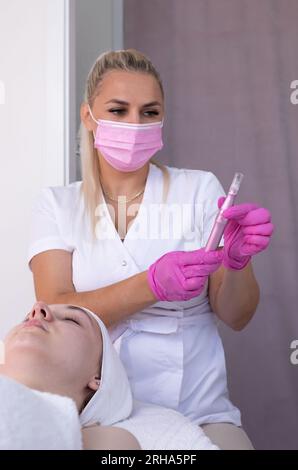 Woman Having Microneedling Treatment, Mesotherapy. Female Cosmetologist Holds Electric Microneedling Pen For Invasive Beauty Procedure Using Thin Stock Photo