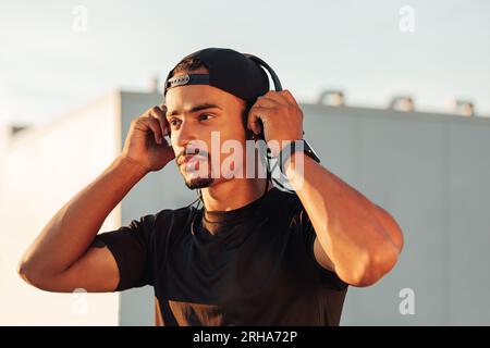Male athlete in cap wearing wireless headphones during outdoor workout Stock Photo