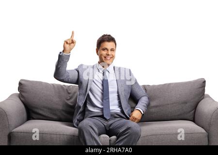 Young man sitting on a gray sofa and pointing isolated on white background Stock Photo