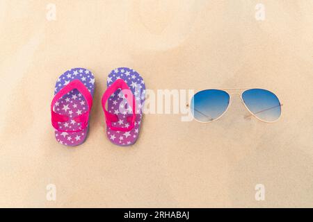 Blue sunglasses and flip flops lie in the sand. Summer vacation, travel and tourism concept. Summer rest. Holiday season Stock Photo