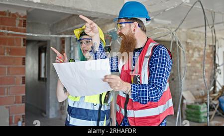 Man and woman builders reading house project speaking at construction site Stock Photo