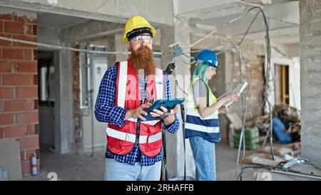 Man and woman builders using touchpad reading house project at construction site Stock Photo