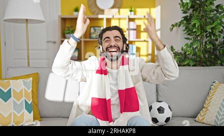 Young hispanic man watching soccer match celebrating at home Stock Photo