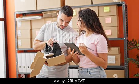 Man and woman ecommerce business workers using touchpad unpacking sneakers on cardboard box at office Stock Photo