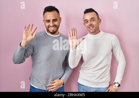 Homosexual couple standing over pink background waiving saying hello happy and smiling, friendly welcome gesture Stock Photo