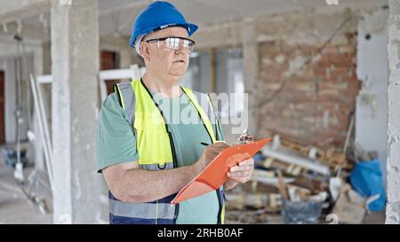 Middle age grey-haired man builder smiling confident writing on clipboard at construction site Stock Photo