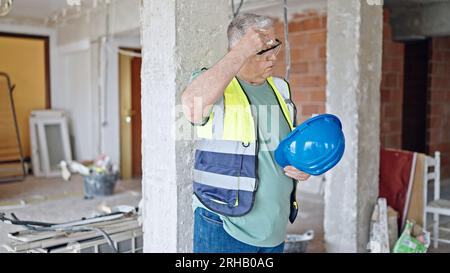 Middle age grey-haired man builder sweating at construction site Stock Photo