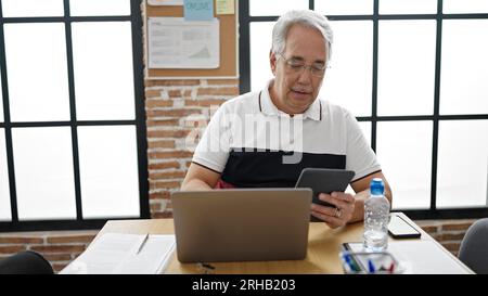 Middle age man with grey hair business worker using touchpad and laptop at office Stock Photo